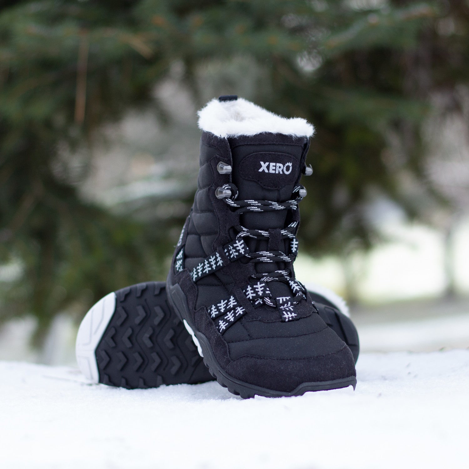 Xero Shoes Alpine Women Black White Trees Barfußschuhe Schneestiefel, getragen in einer Alltagsszene. Leichte, flexible Winterstiefel mit einem stilvollen Baum-Muster, die natürlichen Komfort und Wärme bieten. Erhältlich in unserem Onlineshop für Barfußschuhe.