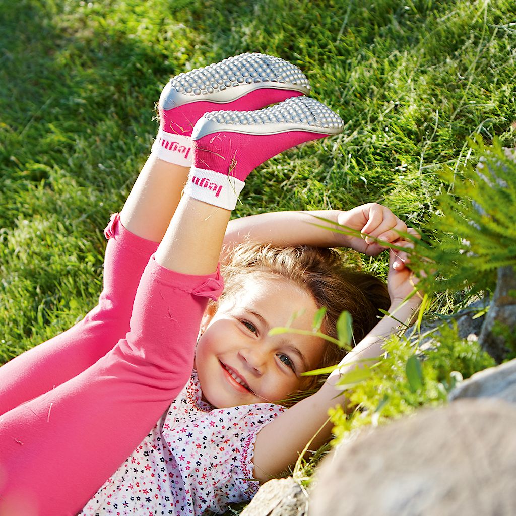 Kind in pinken Barfußschuhen auf einer Wiese